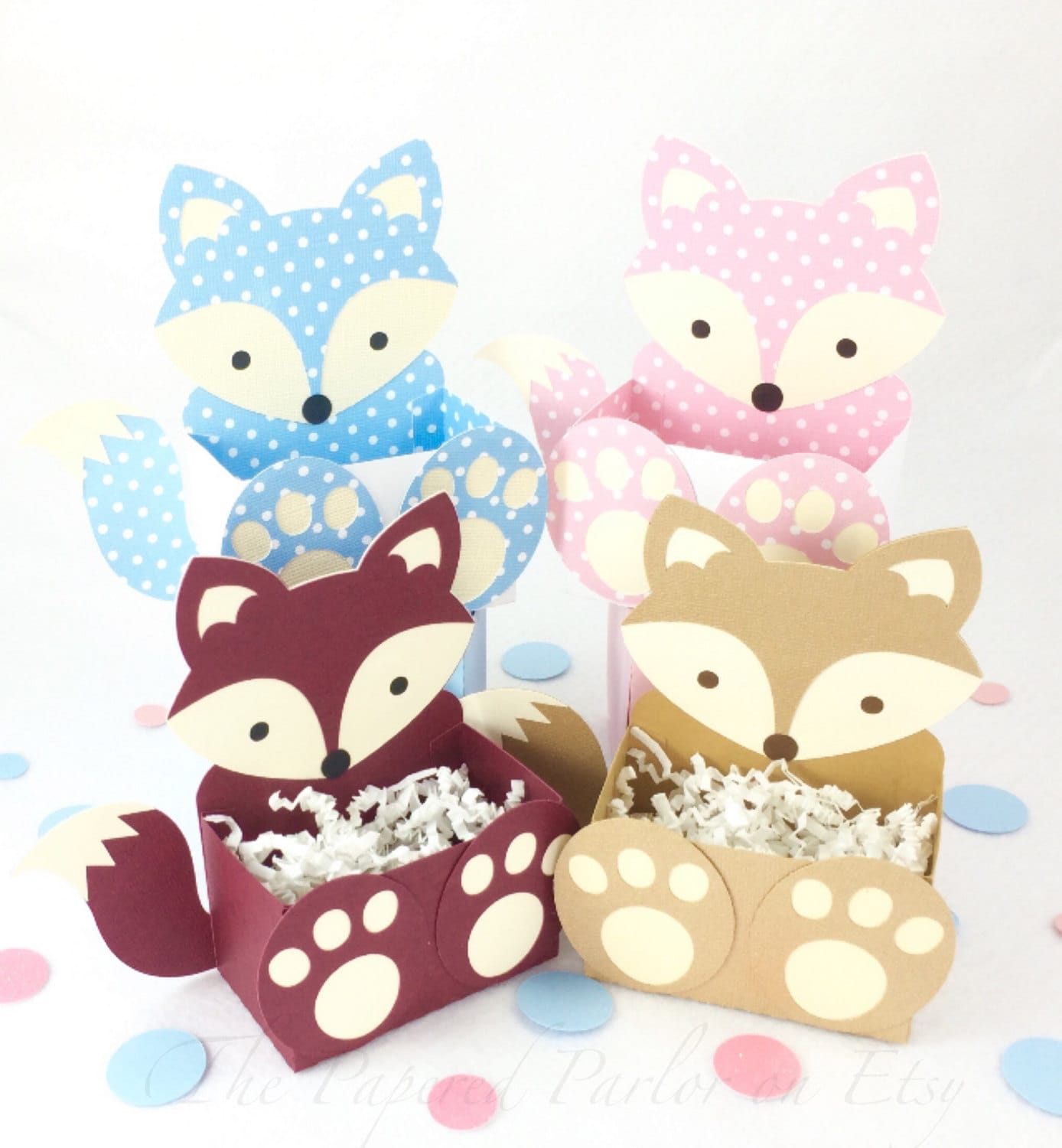 Fox party boxes in a variety of colors that include blue and white polka dot with a cream face, pink and white polka dot with a creams face, maroon with a cream face and golden brown with a cream face. The boxes are adorned with a cute tail and feet.