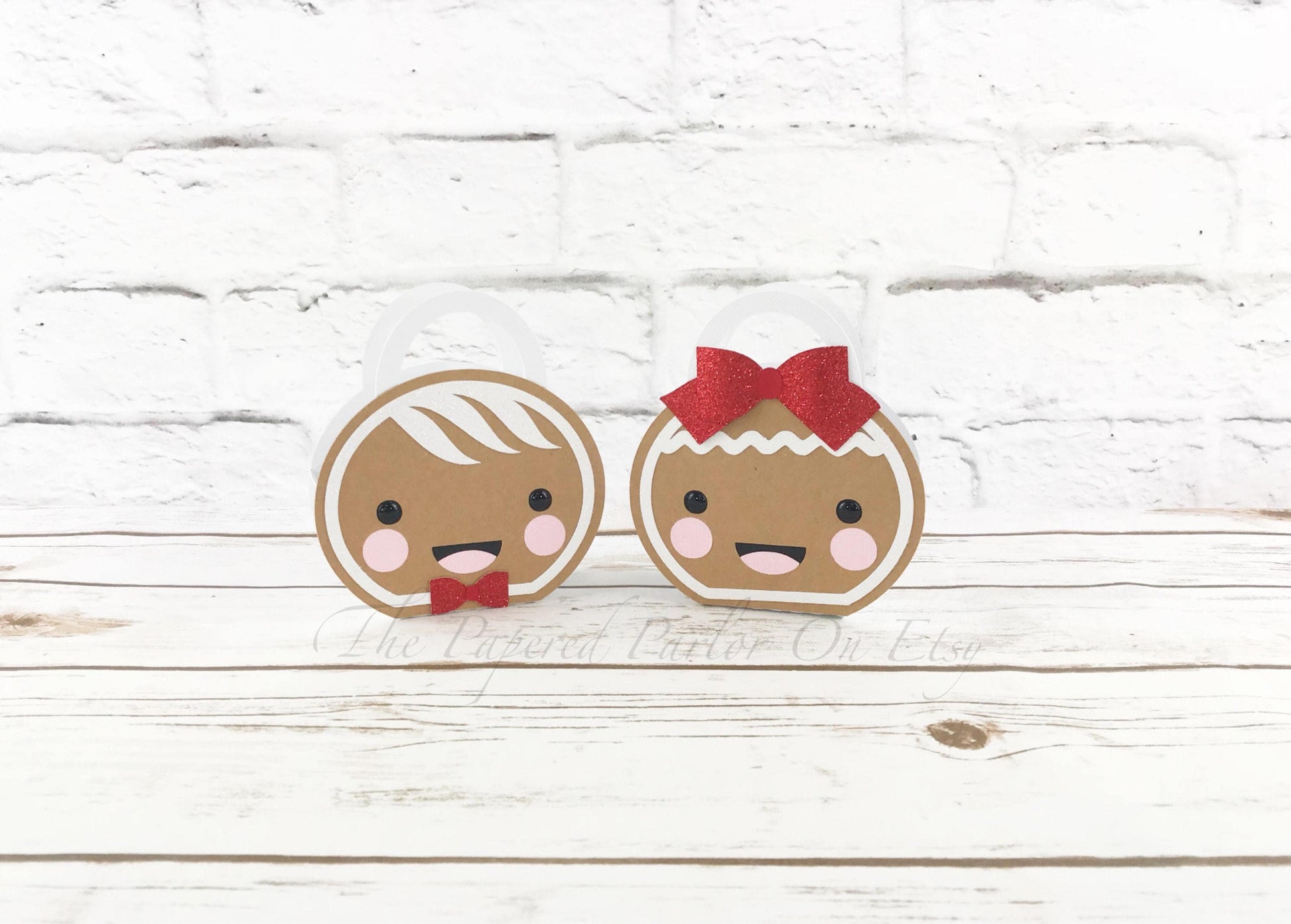 Gingerbread party boxes of a gingerbread boy and gingerbread girl. The gingerbread boy has a bow tie while the girl has a red bow.