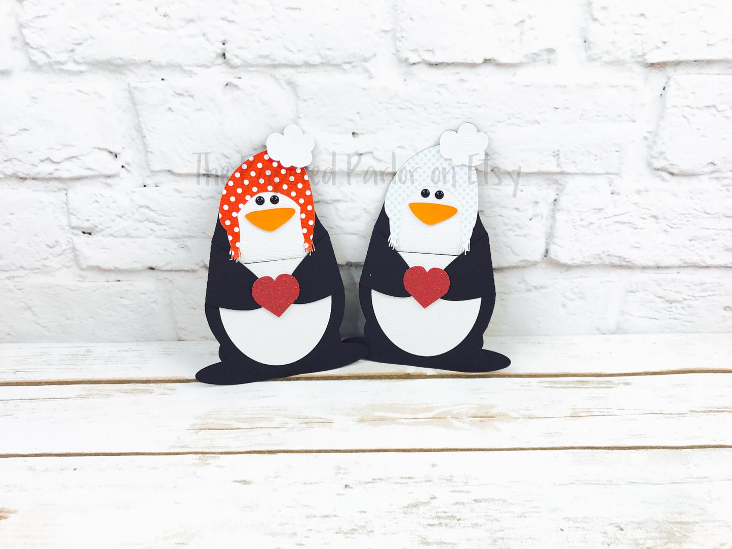 cute penguin candy holders. perfect for bite sized candy. the penguins can be styled with a red polka dot hat or a blue polka dot hat. the penguins are holding hearts with their hands in the middle of their bodies.