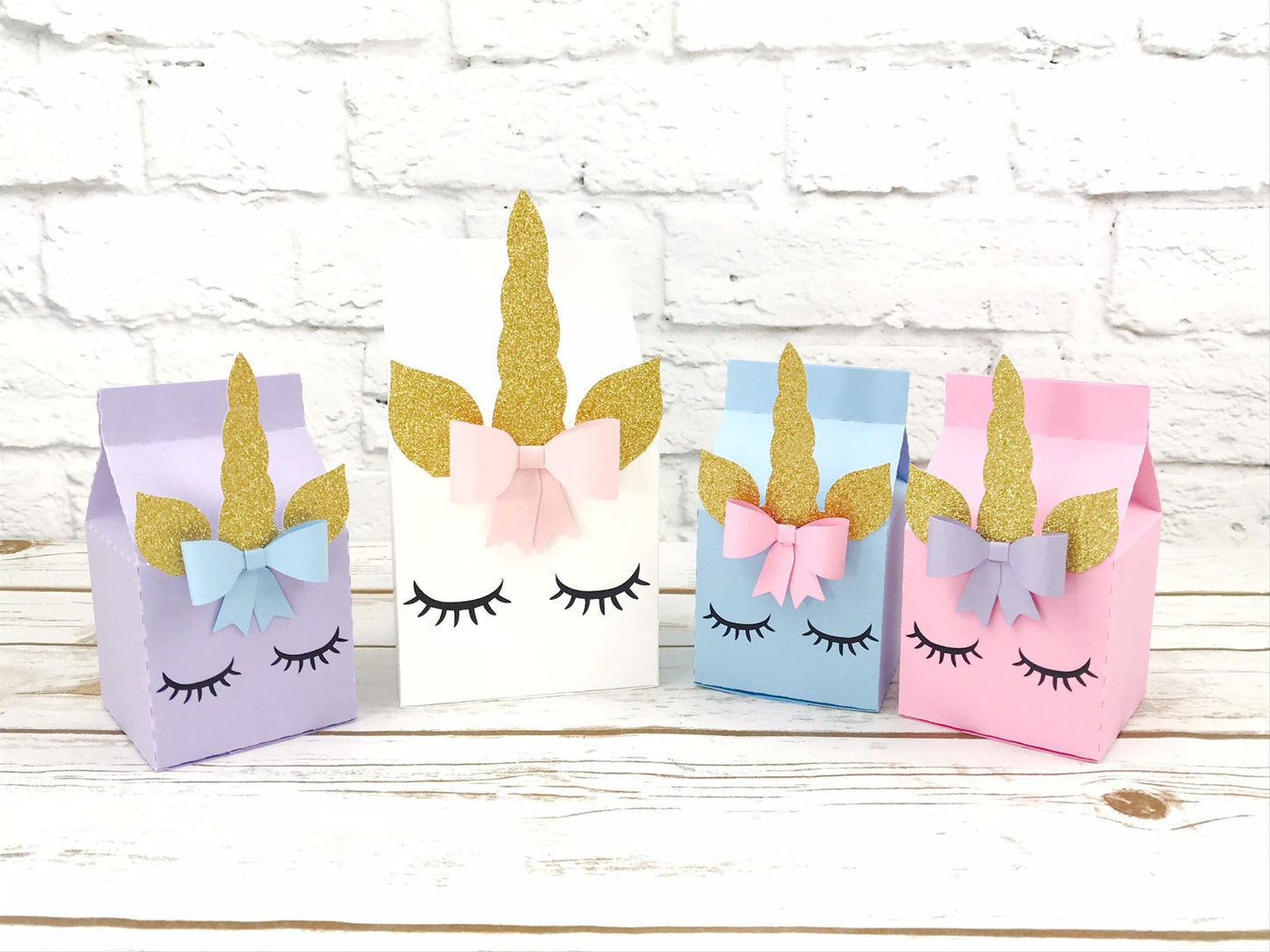 unicorn milk carton party boxes. the unicorn party boxes display a unicorn face with eyelashes, a cute bow near the horn and the ears and horn in glitter gold. the party boxes come in pink, powder blue, white and lavender, in different sizes.