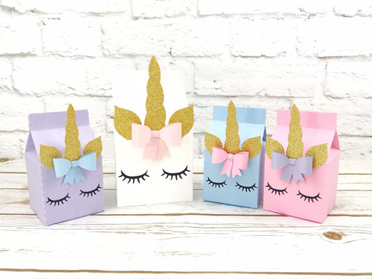 Unicorn milk carton party boxes. The unicorn party boxes display a unicorn face with eyelashes, a cute bow near the horn and the ears and horn in glitter gold. The party boxes come in pink, powder blue, white and lavender, in different sizes.