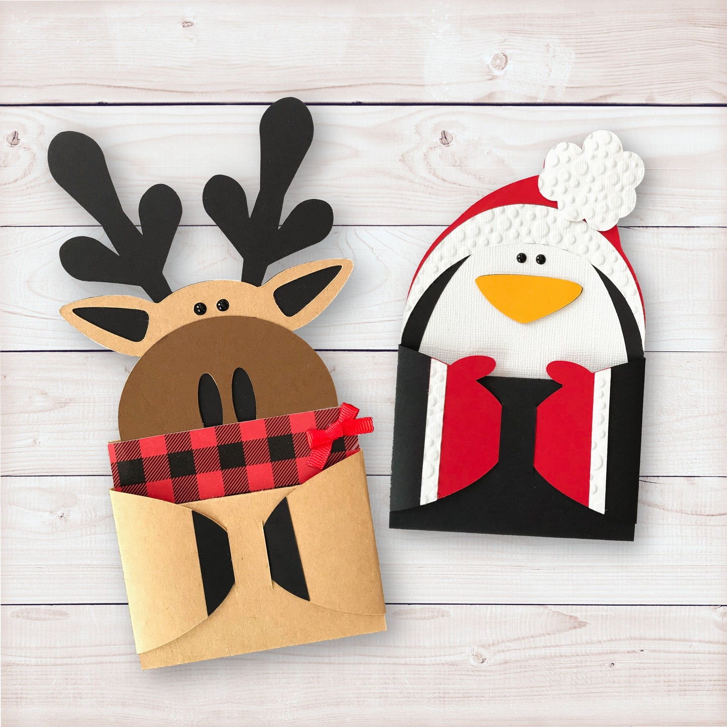 cute moose and penguin gift card holders. the moose is bundle in a buffalo plaid scarf with a little red bow. the penguin gift card holder is in a red hat topped with a white shaped puff ball.